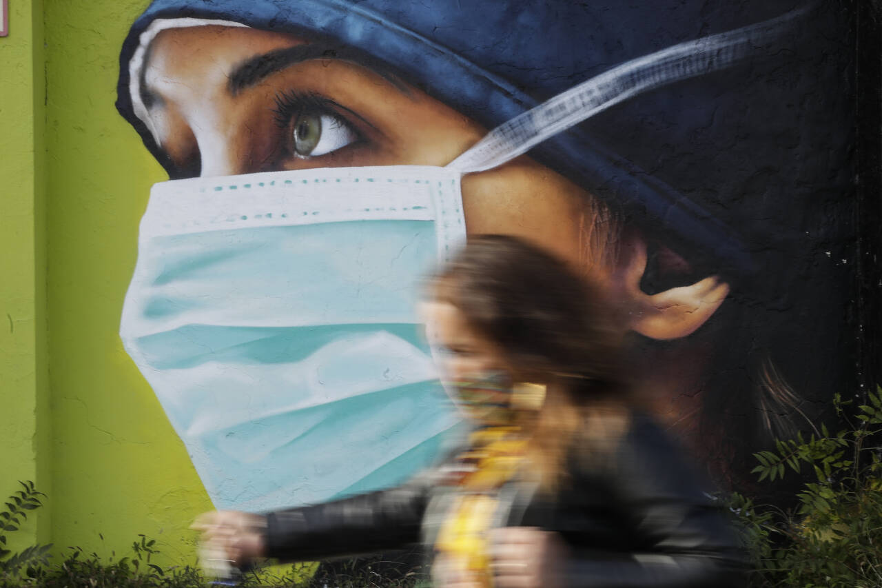 En kvinne går foran et veggmaleri av en sykepleier med munnbind i Milano onsdag denne uken. Italia registrerte onsdag en ny smitterekord. Foto: Luca Bruno/AP/NTB