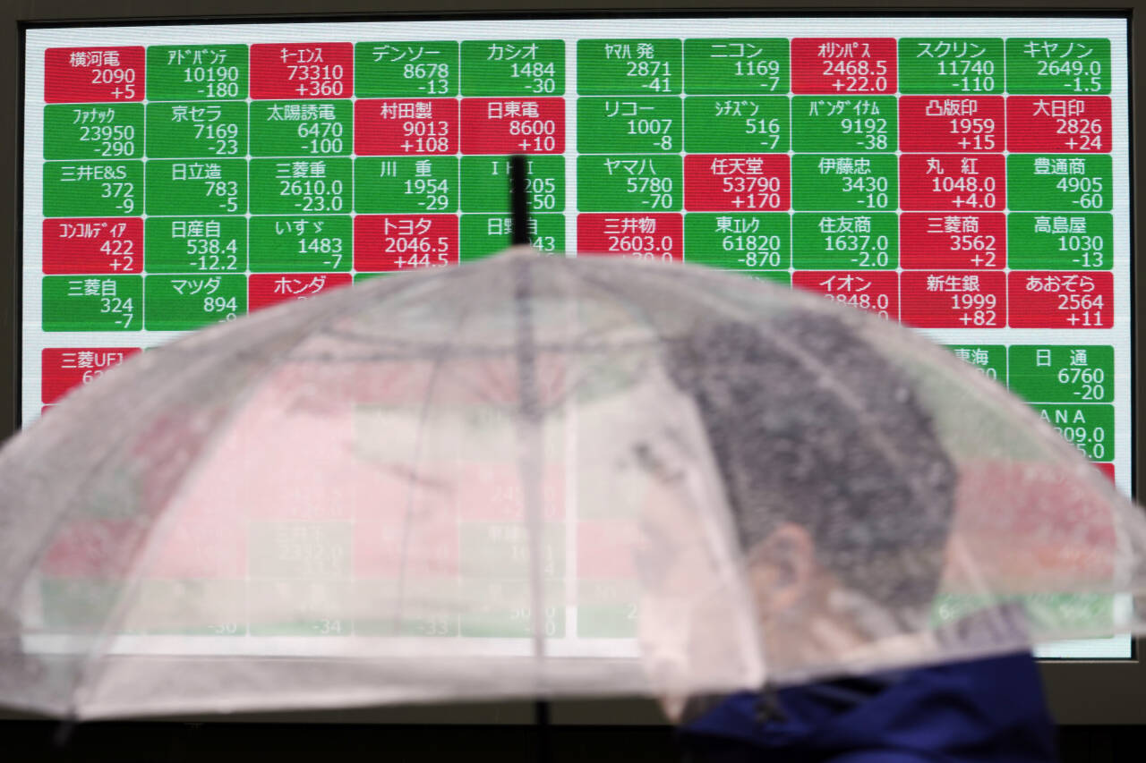 De viktigste børsene i Asia hadde en god handelsdag tirsdag, etter nedgang på Wall Street og i Europa dagen i forveien. Her går en mann med paraply foran en aksjeoversikt i Tokyo. Foto: Eugene Hoshiko / AP / NTB