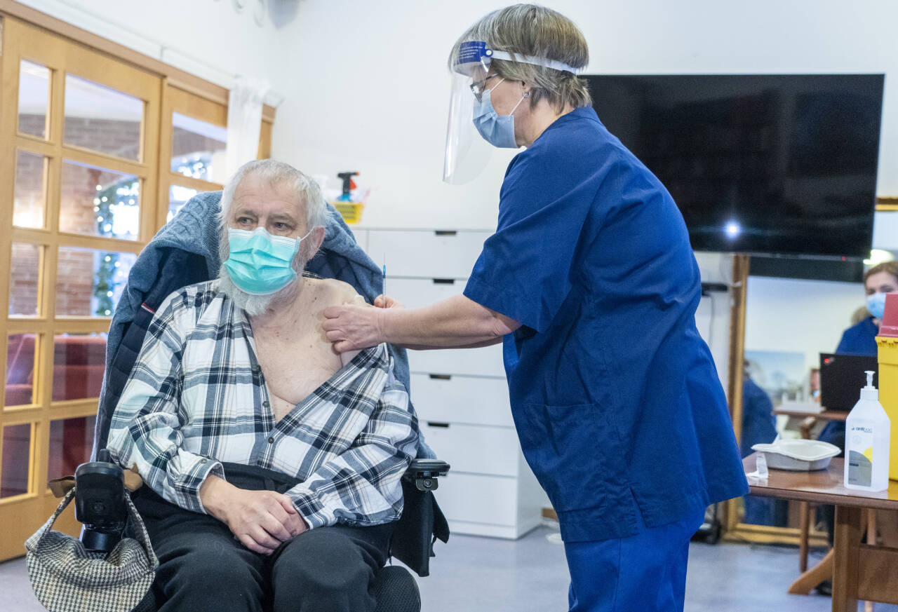 Roger Walter Holland (75) fikk fredag den første Moderna-vaksinen i Norge. Vaksinen ble satt av sykepleier Mone Tshahai Kildal ved Engelborg ressurssenter. Foto: Terje Pedersen / NTB
