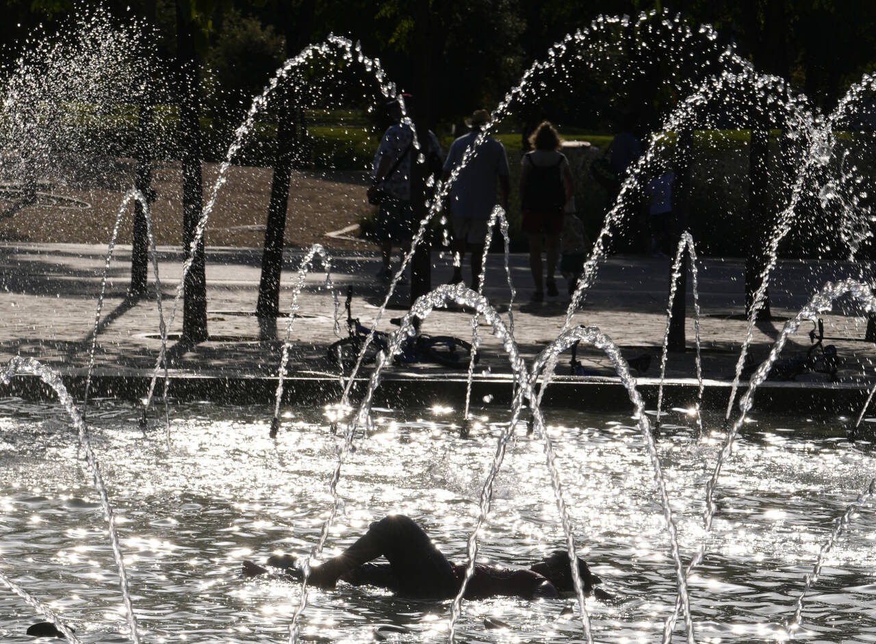 Et barn ligger og kjøler seg ned i en fontene i Spanias hovedstad Madrid. Onsdag legger EU fram sin store pakke med tiltak for å bremse den globale oppvarmingen. Foto: AP / NTB