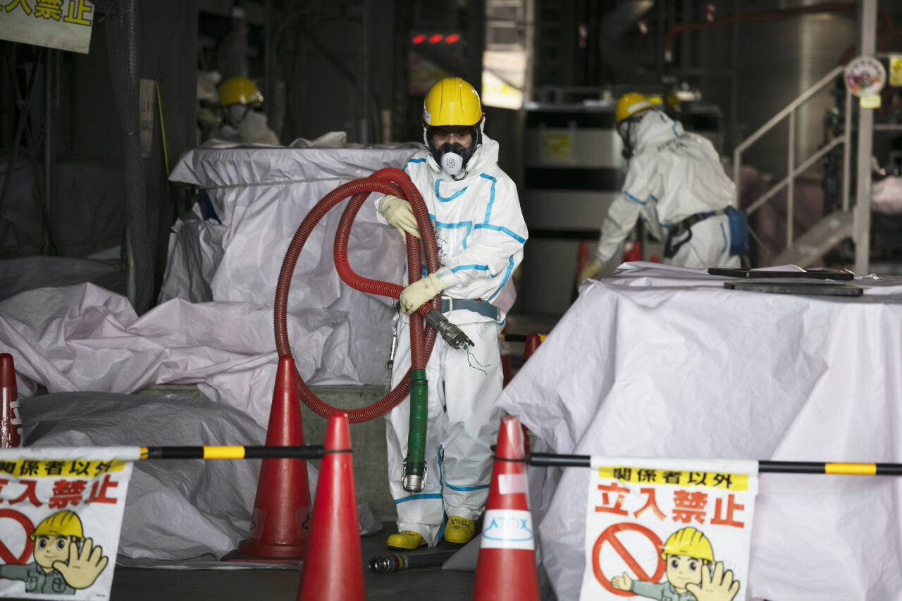 Arbeidere med beskyttelsesdresser jobber ved den ødelagte atomkraftverket Fukushima Daiichi i Japan. Arbeidet med å rydde opp og avvikle atomkraftverket etter katastrofen vil ta 30–40 år og koste enorme beløp. Foto: AP / NTB