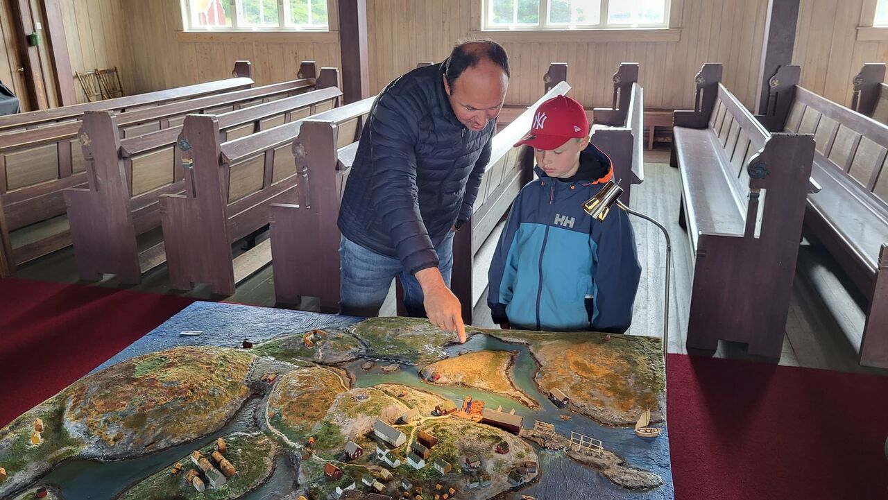 Far og sønn Alf Egil og Joel Nikolai Olsen, som selv bor på fiskeværet Veidholmen studerer hvordan naboene bodde på slutten av 1800 tallet på Brattværet. Modell av Brattværet utstilt i Brattvær kirke. Foto: Vidar Holm