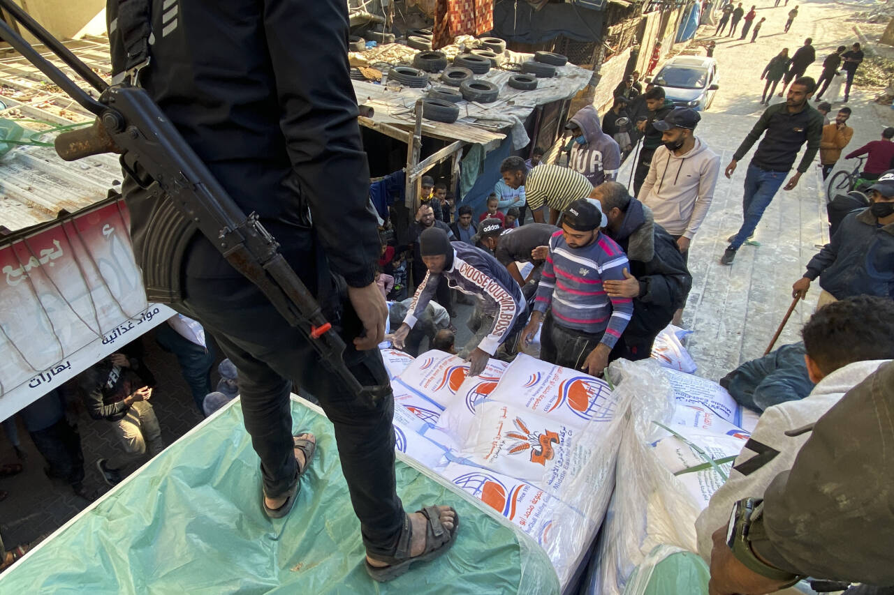 Palestinere losser hvetesekker fra en lastebil til en matvarebutikk og bevoktes av vakt fra Hamas  i Rafah, Gazastripen, tirsdag, 19. desember, 2023. Foto: AP / NTB