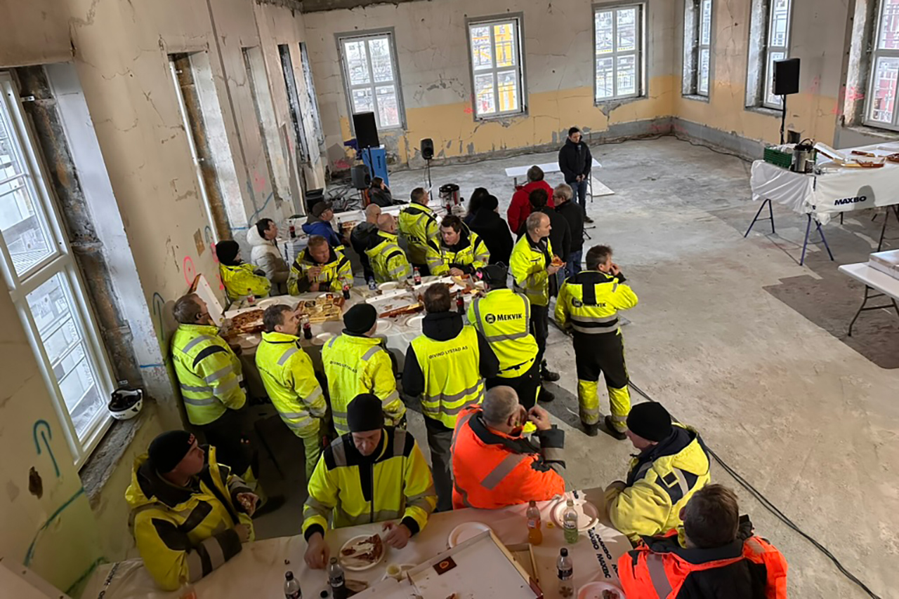 Byggearbeiderne får servert kake og pizza mens operasanger Ole Andreas Silseth synger Helga Natt. Foto: Asgeir Bahre Hansen