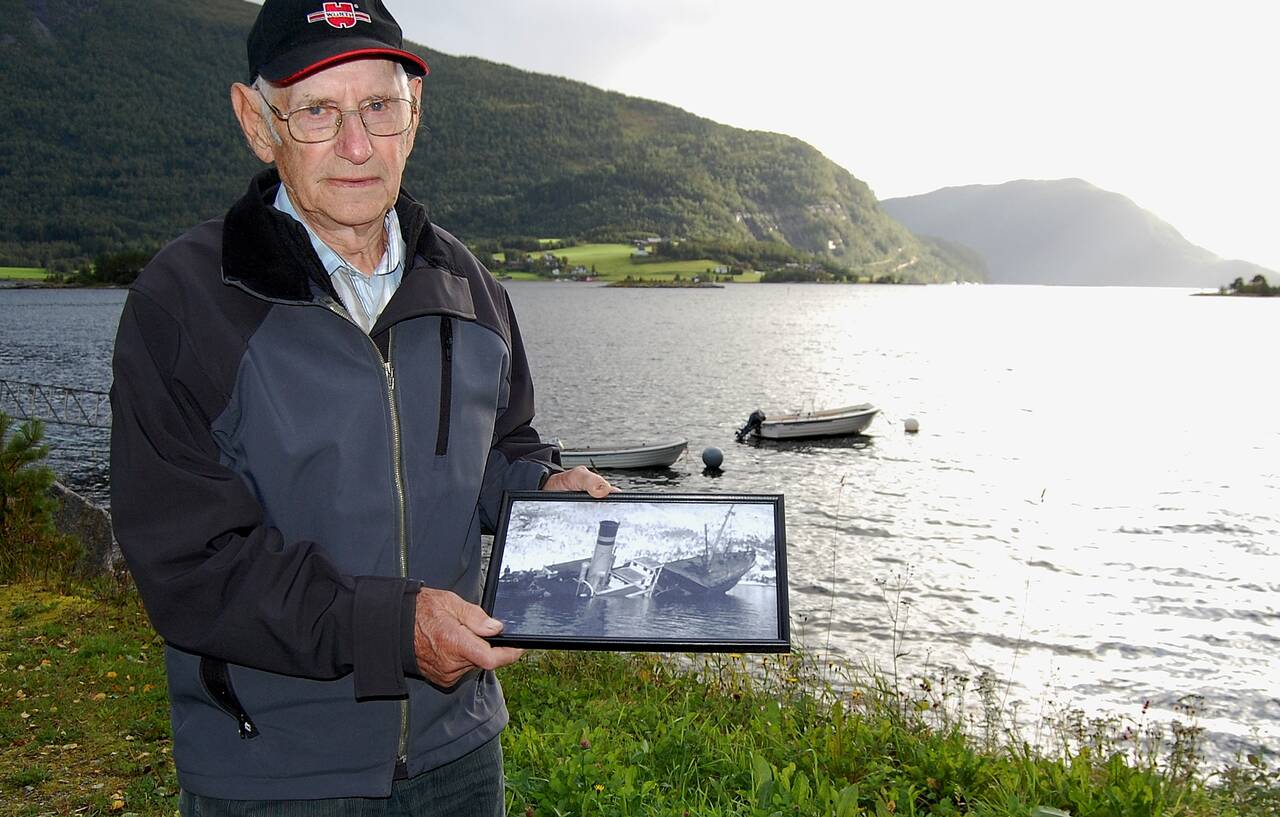 – Ved holmen bak meg forliste rutebåten i mars 1944! Asbjørn var passasjer og viser her foto av havaristen. Foto: Bernt Bøe