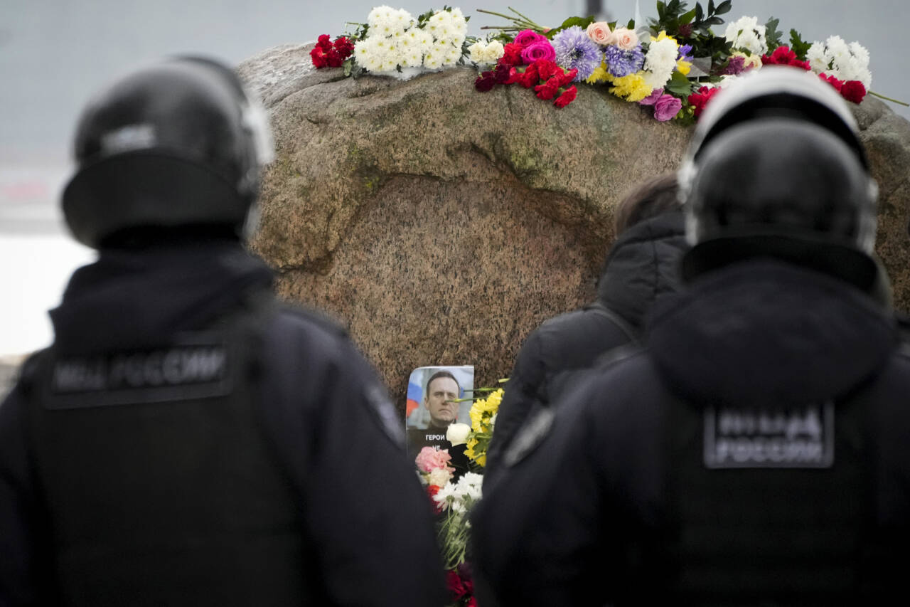 Politifolk holder øye med folk som legger ned blomster for å ære avdøde Aleksej Navalnyj ved et monument i St. Petersburg lørdag. Flere hundre er pågrepet under Navalnyj-markeringer, ifølge en russisk rettighetsgruppe. Foto: Dmitri Lovetsky / AP / NTB