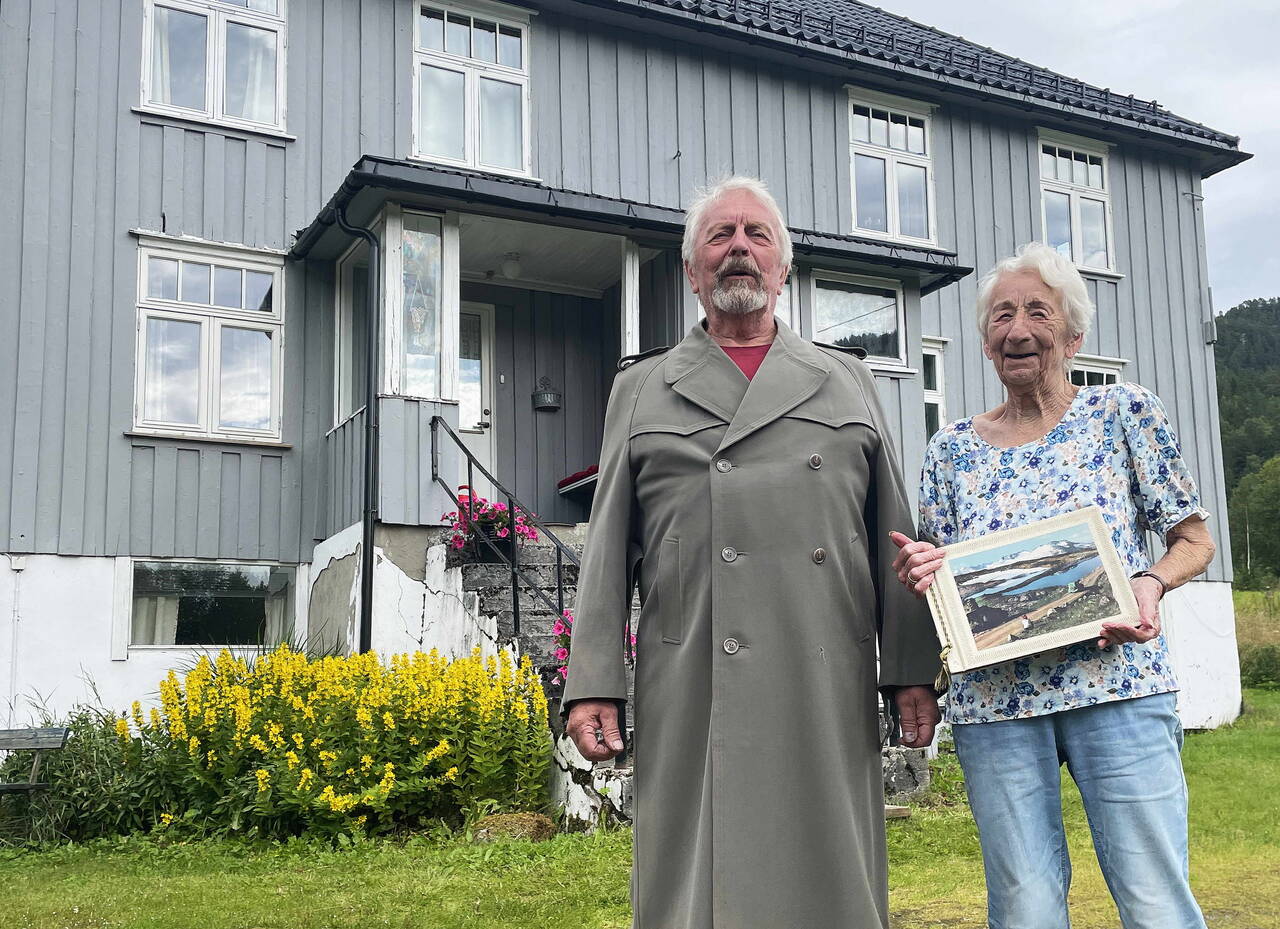 Søskenbarna Geir og Elise Settemsdal framfor «verkstedet» som husa konfeksjonsfabrikk, butikkar og posthus. Geir iført ekte kappe frå fabrikken! Foto: Bernt Bøe