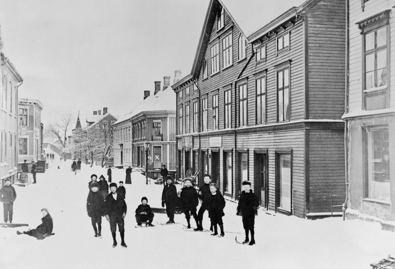 Barn leker med rennarband en vinterdag i den vestlige delen av Storgata på Kirkelandet i Kristiansund. Fra Nordmøre museums fotosamlinger.