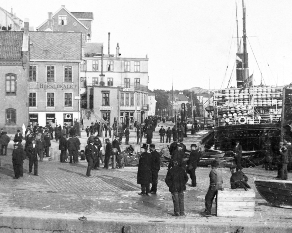 Tollflagg med sildesalat på Tollbua, Kristiansund ca 1900. Damskip med tønner på dampskip enten tomme eller full av sild til eksport. Fra Nordmøre museums fotosamlinger.