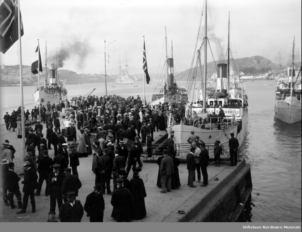 Et bilde fra Piren med store folkemengder på Kirkelandet i Kristiansund, hvor vi ser 4 dampbåter enten ved kai eller er i ferd med å ankomme havnen. Det ene dampskipet som vi ser ved kai, er "D/S Statsraad Riddervold". Bildet er tatt mellom 1920 og 1925. Fra Nordmøre Museums fotosamlinger.